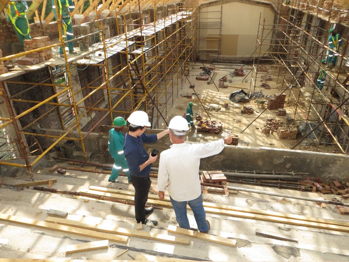 Dois profissionais de capacete conversando em um canteiro de obras com andaimes